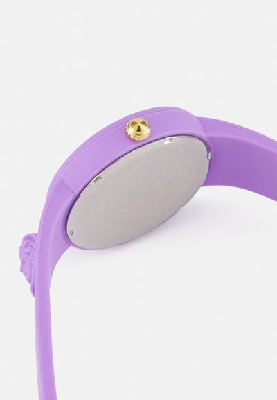 Vijolična silikonasta ura z okroglo ohišjem in zlatim krono. Zadaj ima srebrno površino z odtisnjenim vzorcem.