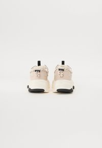 Beige joggesko med en glatt overdel, svart såle og vevde lisser. Har trekkfliker og polstret krage for komfort.
