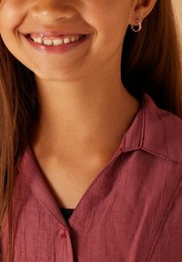 Chemise boutonnière maroon, texturée, avec un col et un design plissé ; petites boucles d'oreilles en argent avec des accents colorés.