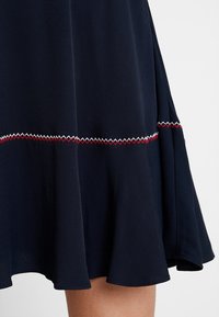 Ourlet de jupe bleu marine avec détail de couture zigzag rouge et blanche au-dessus d'un tissu ample et évasé s'arrêtant au-dessus du genou.