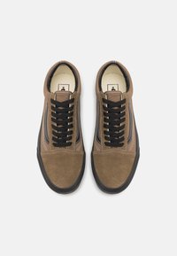 Hnědé semišové tenisky s černými tkaničkami, s černým pruhem podél boků a strukturovanou podrážkou. Klasický nízký profil.