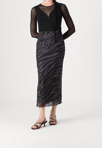 Haut noir à manches longues avec panneau transparent, associé à une jupe mi-longue à imprimé zèbre noir et gris, finie par un ourlet en forme de vagues.