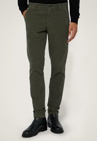 Olivgröna byxor i slim fit-design, tillverkade av bomullstyg med struktur. Matchas med svarta ankelboots med en slät yta.