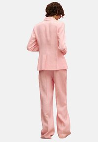 Light pink tailored suit, featuring a structured jacket with a small vent, wide-legged trousers, and a smooth fabric texture.