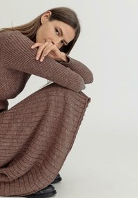 Strickkleid in gedämpften Brauntönen mit vertikalen Rippen; lange Ärmel, Rundhalsausschnitt und einem fließenden Rock, der sanft bis zum Boden fällt.