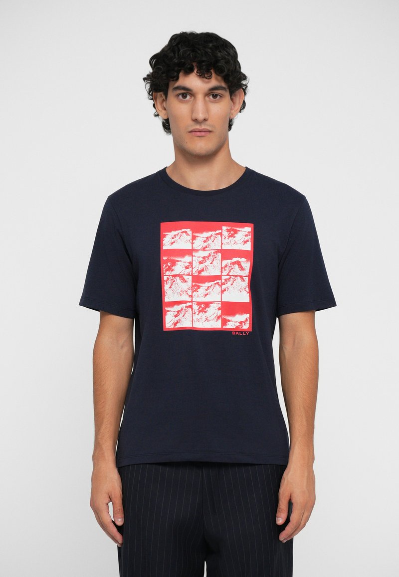 Camiseta de algodón azul marino con un diseño de cuadrícula de bloques de impresión de montañas rojas, mangas cortas y cuello redondo. Texto "BALLY" en la esquina inferior.