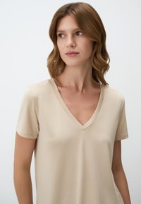 T-shirt beige a maniche corte con scollo a V realizzato in tessuto morbido, caratterizzato da una vestibilità comoda e una superficie liscia. Design minimalista senza decorazioni.