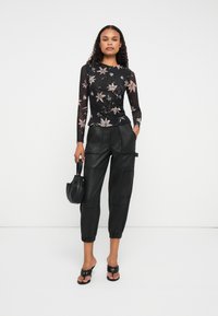 Top negro de manga larga con estampado floral, combinado con pantalones cargo recortados de cuero negro y un bolso pequeño negro. Sandalias con tacón bloque.