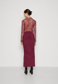 Mauve průsvitná halenka s dlouhým rukávem a vzorem srdcí, spárovaná s přiléhavou bordó sukní se zřasením a černými platformovými botami.