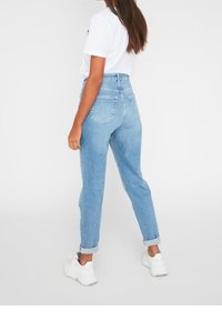 Jeans azzurri a vita alta in taglio dritto, con risvolti e due tasche posteriori. Abbinati a sneakers bianche e una t-shirt semplice.