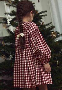 Vestido de cuadros rojos y blancos con mangas globo y cintura ajustada. La parte trasera cuenta con una apertura en forma de llave y un pequeño lazo crema como acento.