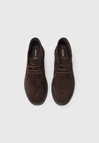 Brown suede shoes with a smooth texture, rounded toe, and traditional lacing. Notable Geox branding on the insole.