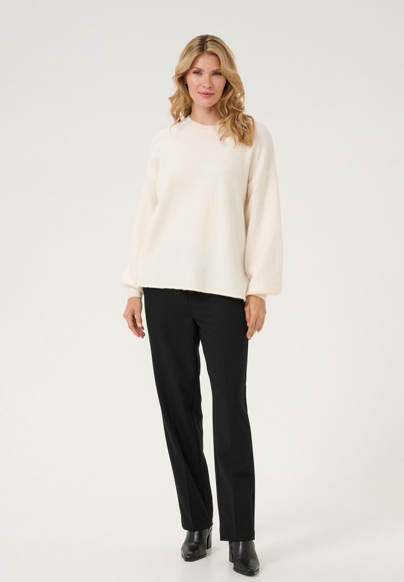 Maglione fluffy color crema con scollatura rotonda e maniche ampie, abbinato a pantaloni neri aderenti e stivali neri alla caviglia.