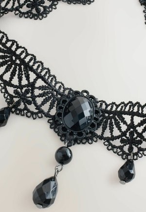 Black lace choker featuring a central faceted black stone with decorative metal accents, and hanging black bead details. Intricate lace design.