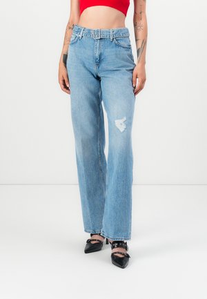 Jeans a gamba larga di color blu chiaro con una toppa strappata sulla coscia sinistra, con vita con cintura. Abbinati a tacchi a punta nera.