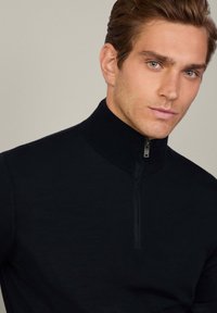 Svart zip-up tröja med hög krage och ribbat mönster. Har en subtil dragkedjedetalj vid halsen. Åtsittande design.