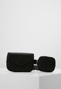 Sac en cuir noir avec fermeture à rabat et pochette carrée amovible, présentant une texture lisse et des accents de métal argenté. Design compact.