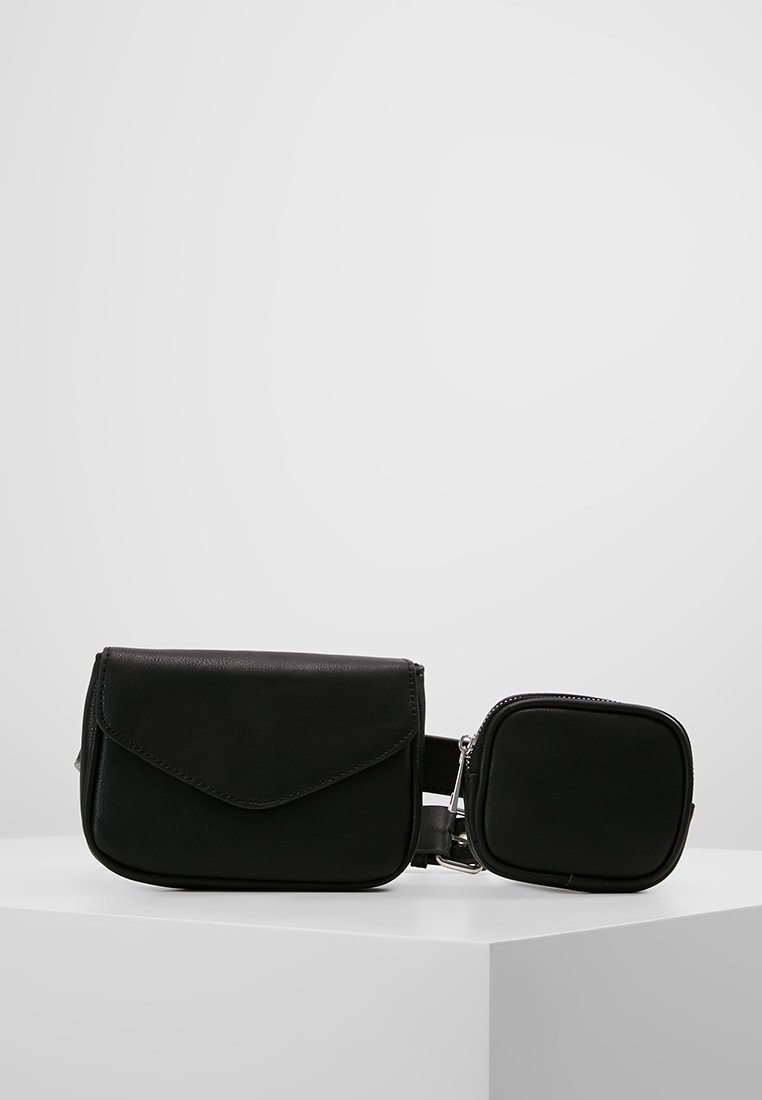 Sac en cuir noir avec fermeture à rabat et pochette carrée amovible, présentant une texture lisse et des accents de métal argenté. Design compact.