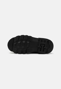 Semelle de chaussure en caoutchouc noir avec des profondes rainures et un motif "H" en relief au talon, conçue pour une bonne adhérence sur surfaces lisses.