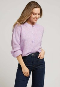 Gilet en tricot lavande avec un col rond, texture côtelée et cinq boutons assortis, associé à un jean taille haute en denim foncé.