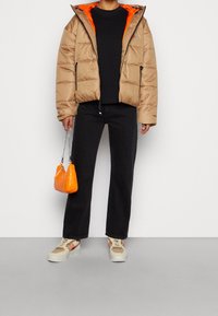 Puffjacka i beige med en orange inredning, svart topp, svarta vida jeans, orange quiltad handväska och flerfärgade sneakers.