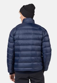Giacca puffa blu navy con design a cuciture orizzontali, colletto alto e polsini elastici. Abbinata a un berretto a maglia nero.