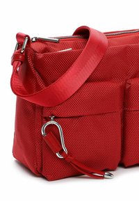 Punane tekstureeritud riidest õlakott lai rihmaga, esiküljel tõmblukuga tasku ja metallist karabiinkinnitusega, mis on kinnitatud nahast aasale.