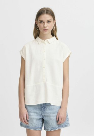 Light cream, short-sleeve shirt with a button-down front and collar; features a textured fabric and a straight hem, paired with denim shorts.