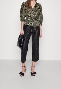 Blouse à imprimé léopard avec un col en V, taille cintrée ; associée à un pantalon en cuir noir court et des talons noirs ornés de nœuds.