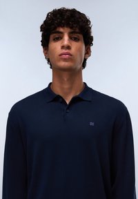 Polo a maniche lunghe blu navy realizzato in morbido cotone, con patta a due bottoni e un piccolo logo ricamato sul petto sinistro.