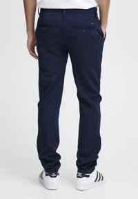 Temno modri hlače s slim fit krojem, z gladko teksturo in dvema zadnjima žepoma s gumbi, v kombinaciji z belimi športnimi copati.