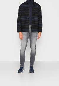 Svart och marinrandig skjorta med två bröstfickor, kombinerad med grå slim fit jeans och marinblå sneakers med vita accenter.