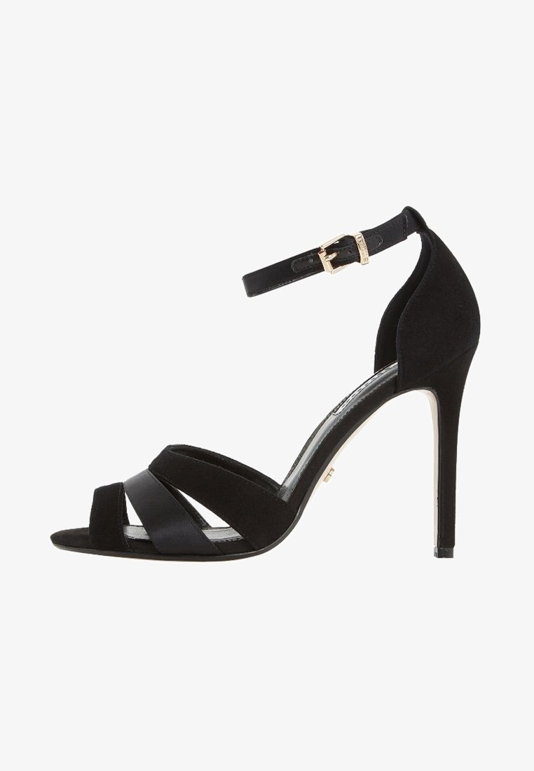 Sandale à talons hauts en suède noir avec un open toe, dotée de brides croisées et d'une sangle ajustable à la cheville avec des accessoires en métal doré.
