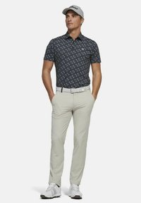 Korte mouwen, donkerblauwe polo met een geometrisch patroon en kraag, gecombineerd met lichtbeige broek en witte golfschoenen. Grijze pet gedragen.