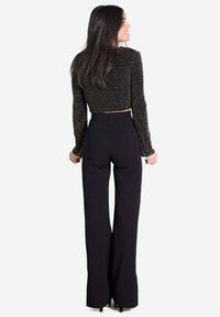 Pantalons noirs évasés associés à un haut noir court avec des éclats dorés. Les manches longues et les détails en tissu texturé rehaussent le design.