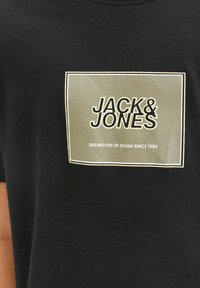 Zwart katoenen T-shirt met een rechthoekige groene afbeelding met de tekst "JACK & JONES" en "DEFINITION OF DENIM SINCE 1990".
