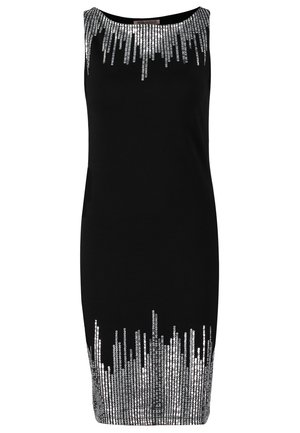 Frau, die ein ärmelloses schwarzes Kleid mit silbernen Paillettenmustern am Ausschnitt und Saum trägt, schwarze transparente Strumpfhosen, schwarze Absätze und eine schwarze Clutch in der Hand hält.