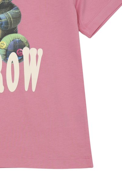 T-shirt rosa con una grafica di personaggi sorridenti e colorati sovrapposti, con la parola "Grow" in lettere bianche in grassetto. Materiale in cotone morbido.