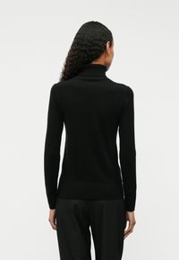 Fekete garbónyakú pulóver, puha kötött anyagból készült, hosszú ujjakkal és testhezálló szabással, bordázott szegéllyel és gallérral.