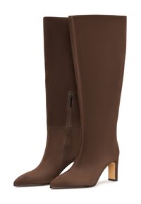 Botas marrones de tacón alto hechas de tela suave, con punta en forma de pico y cremallera lateral. El tacón es de un color claro que contrasta.