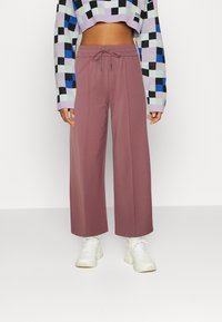 Calças largas em tom mauve claro com cintura elástica e cordão. Combinadas com um suéter cropped de padrão quadriculado multicolorido e sapatilhas brancas.