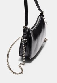 Borsa a mano in pelle nera con un design curvo, dotata di una tracolla in catena argentata e chiusura con zip, che mette in mostra una texture liscia e lucida.