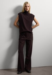 Dunkelbrauner ärmelloser Rollkragenpullover kombiniert mit passenden weit geschnittenen Hosen. Die Stricktextur steht im Kontrast zu dem glatten Stoff und sorgt für eine lässige Silhouette.