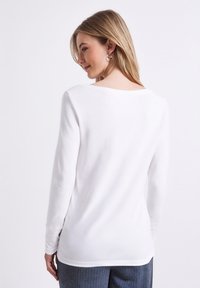 Langærmet hvid skjorte med rund hals, glat tekstur og en afslappet pasform. Billedet viser ryggen og fremhæver det enkle design.