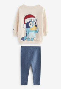 Sweter w jasnym beżu z nadrukiem postaci z kreskówki; niebieskie legginsy. Miękka tkanina, luźny krój, okrągły dekolt, ściągacze, gładkie ciemnoniebieskie nogawki.