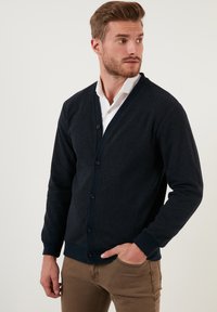 Jūras spēku cardigan ar V-veida kakla izgriezumu, pogu aizdari un ribotām piedurknēm. Izgatavots no adīta auduma, apvienots ar baltu krekla kreklu zem tā.