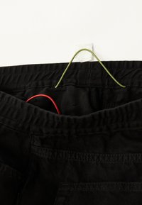 Pantalones negros con una cinturilla elástica colgados de un gancho. Un cordón rojo visible dentro de la cinturilla. La tela parece suave con una textura sutil.