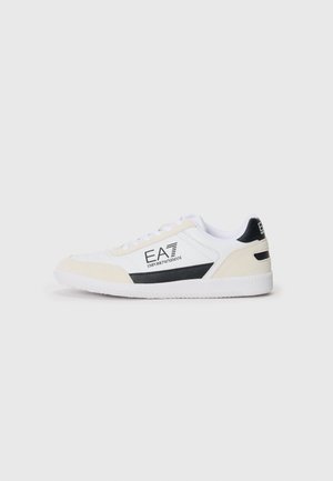 White sneaker with beige suede accents, black logo, and rubber sole. Features flat lace-up design and textured side panel.