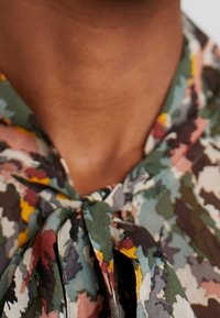 Multikleuren blouse met een bloemenpatroon in tinten groen, roze en geel. Het heeft een strikdetail bij de hals. Zachte, lichte stof.