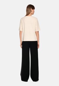 Cream-colored short-sleeve top with a straight cut, paired with black wide-leg pants featuring a side zipper detail.